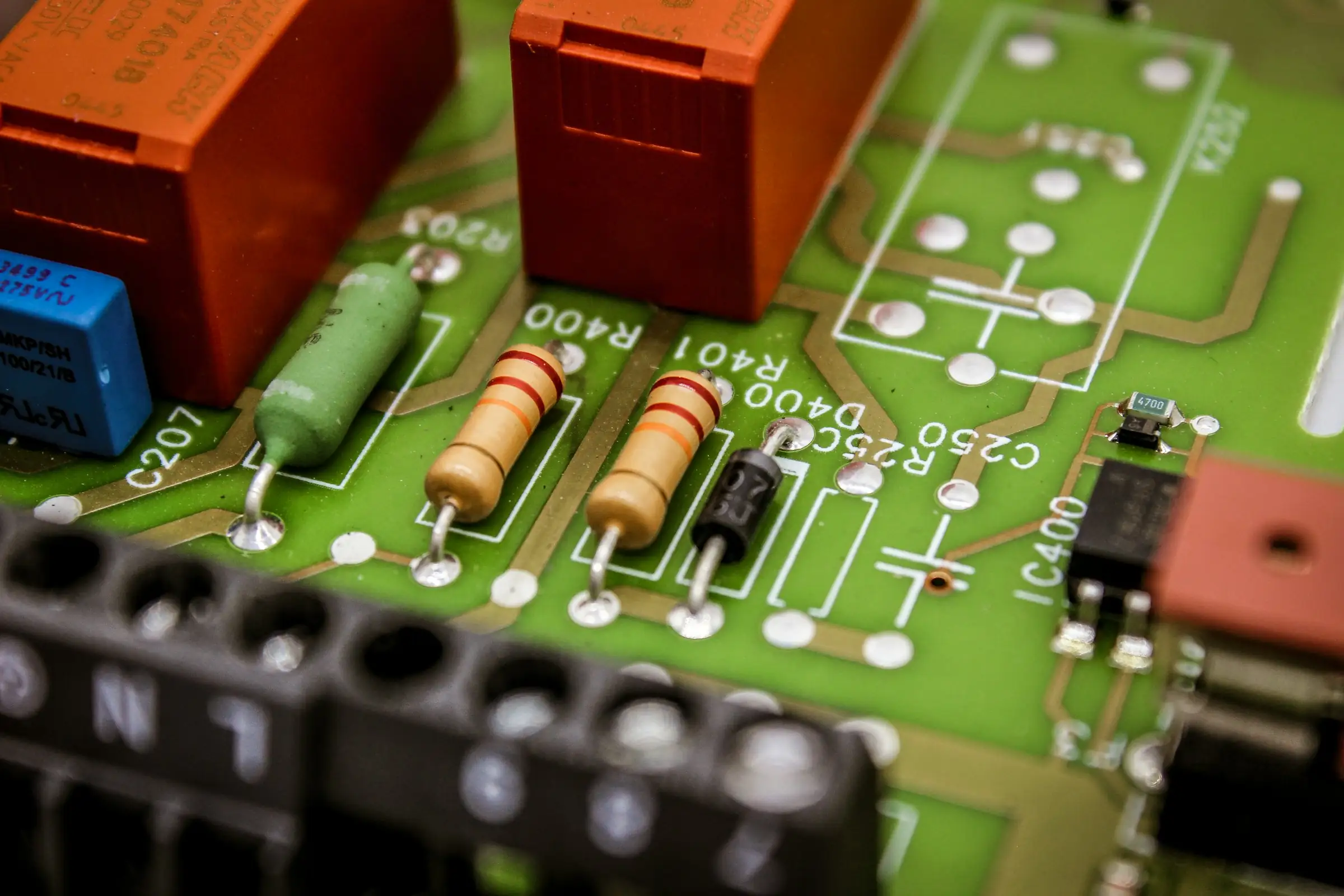 Close-up of resistors, relays and a terminal block on a green circuit board