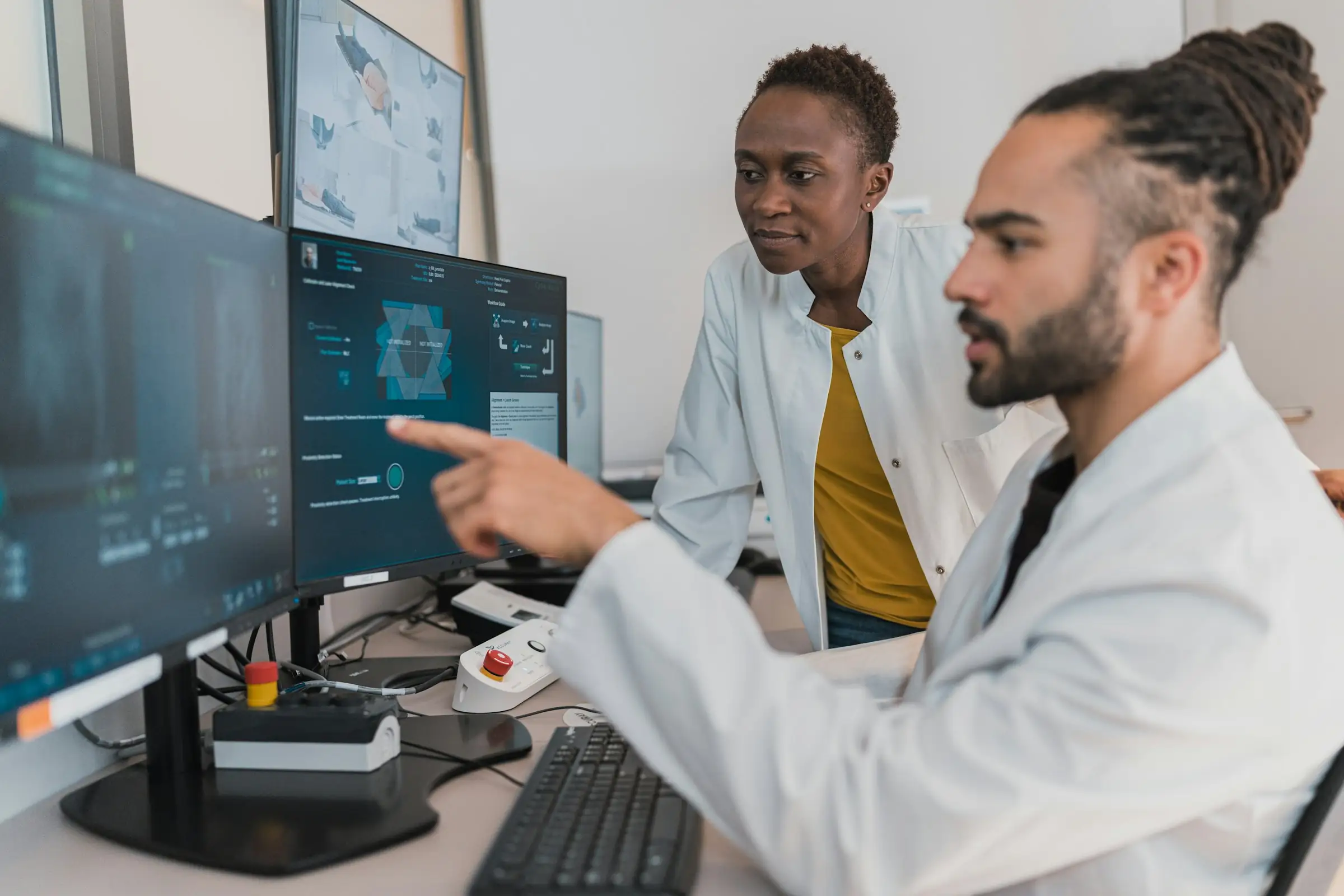 Two clinicians in white coats reviewing medical software on desktop monitors