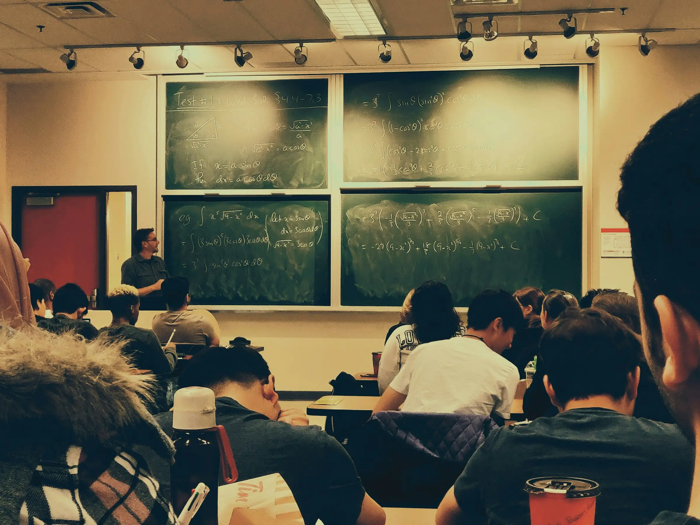 University lecture hall with students facing a professor at chalkboards