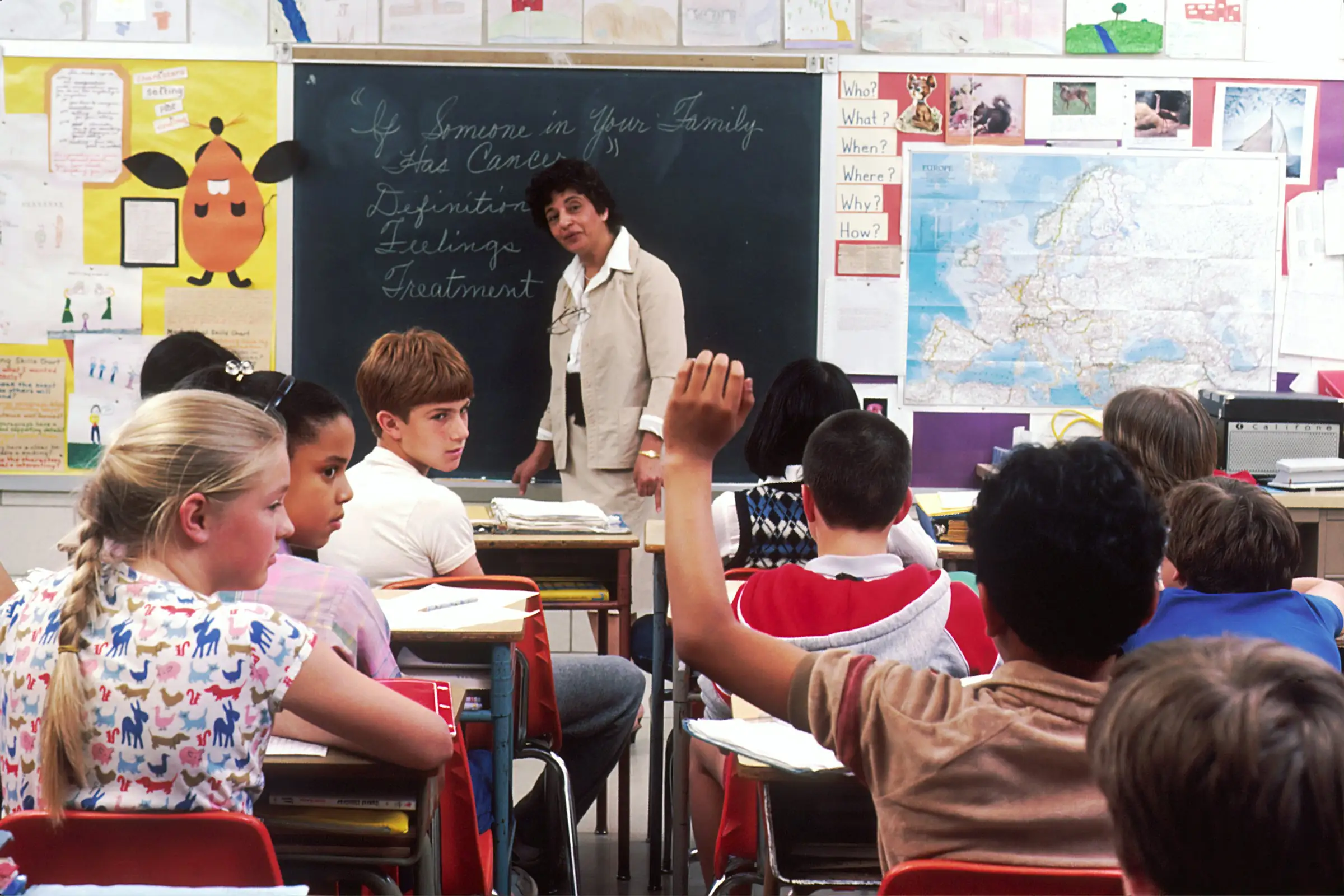 Teacher at a chalkboard with elementary students raising hands in a classroom