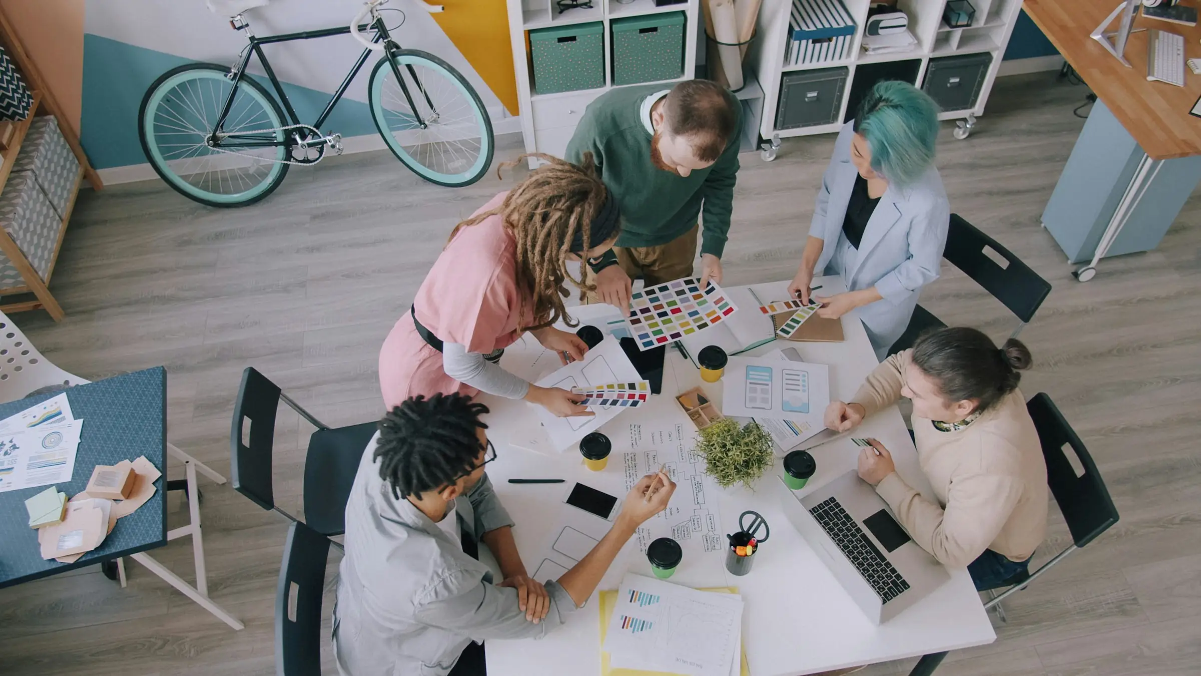 Overhead view of a creative agency team working around a table with color swatches and layouts