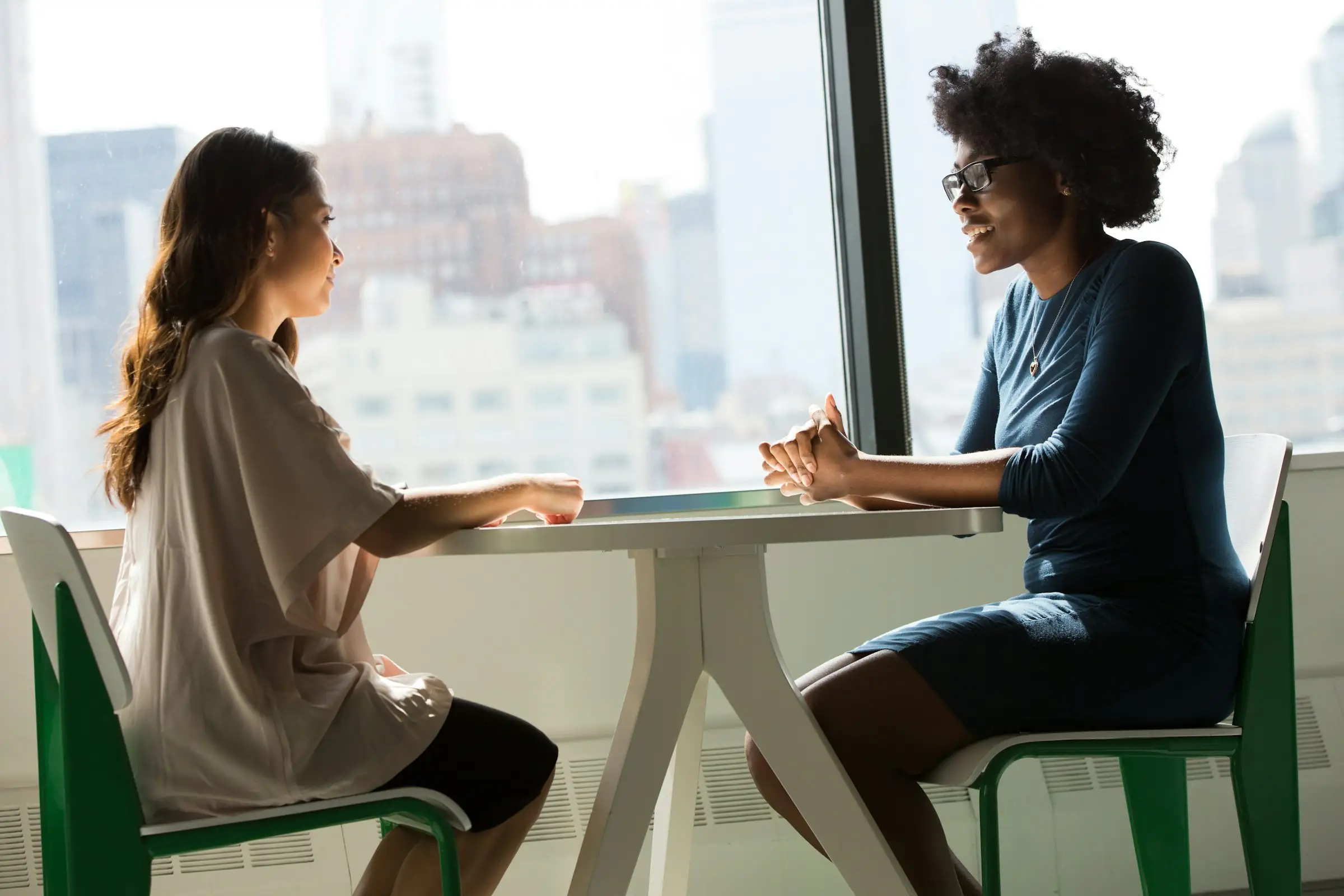 Two people in a job interview at a small table by an office window